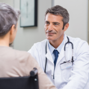 A doctor in a white coat with a stethoscope talking to a patient in an office.