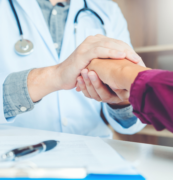 Doctor in white coat with stethoscope shaking hands with patient over a desk with paperwork.